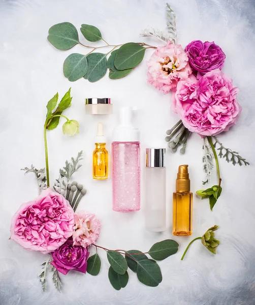 This picture shows several cosmetic bottles and jars placed on a light background.
They are surrounded by pink flowers and green leaves, arranged in a pretty frame.
